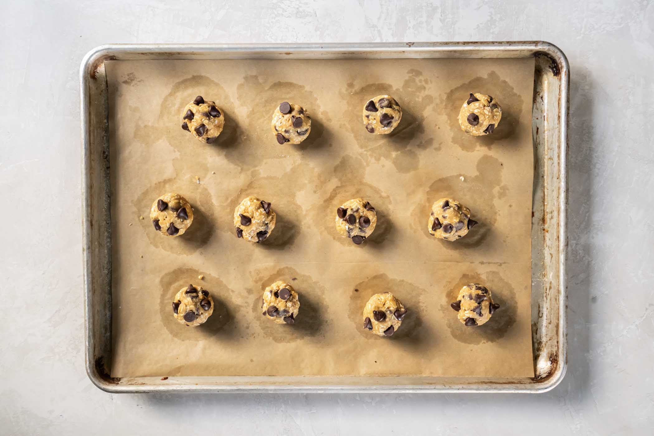 Extra chocolate chips pressed into raw cookie dough balls on baking sheet.
